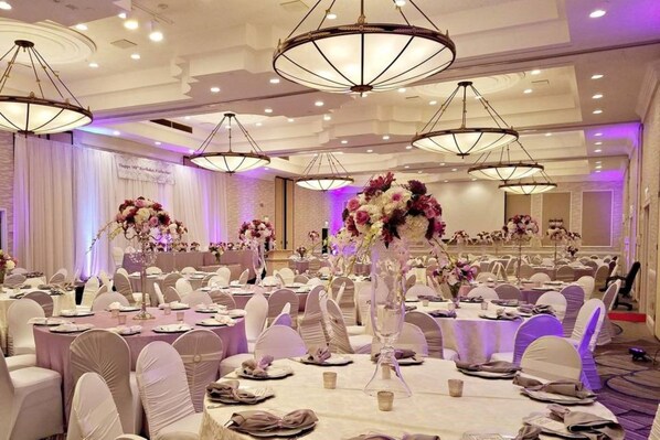 A banquet hall with round tables, white chairs, and floral centerpieces.