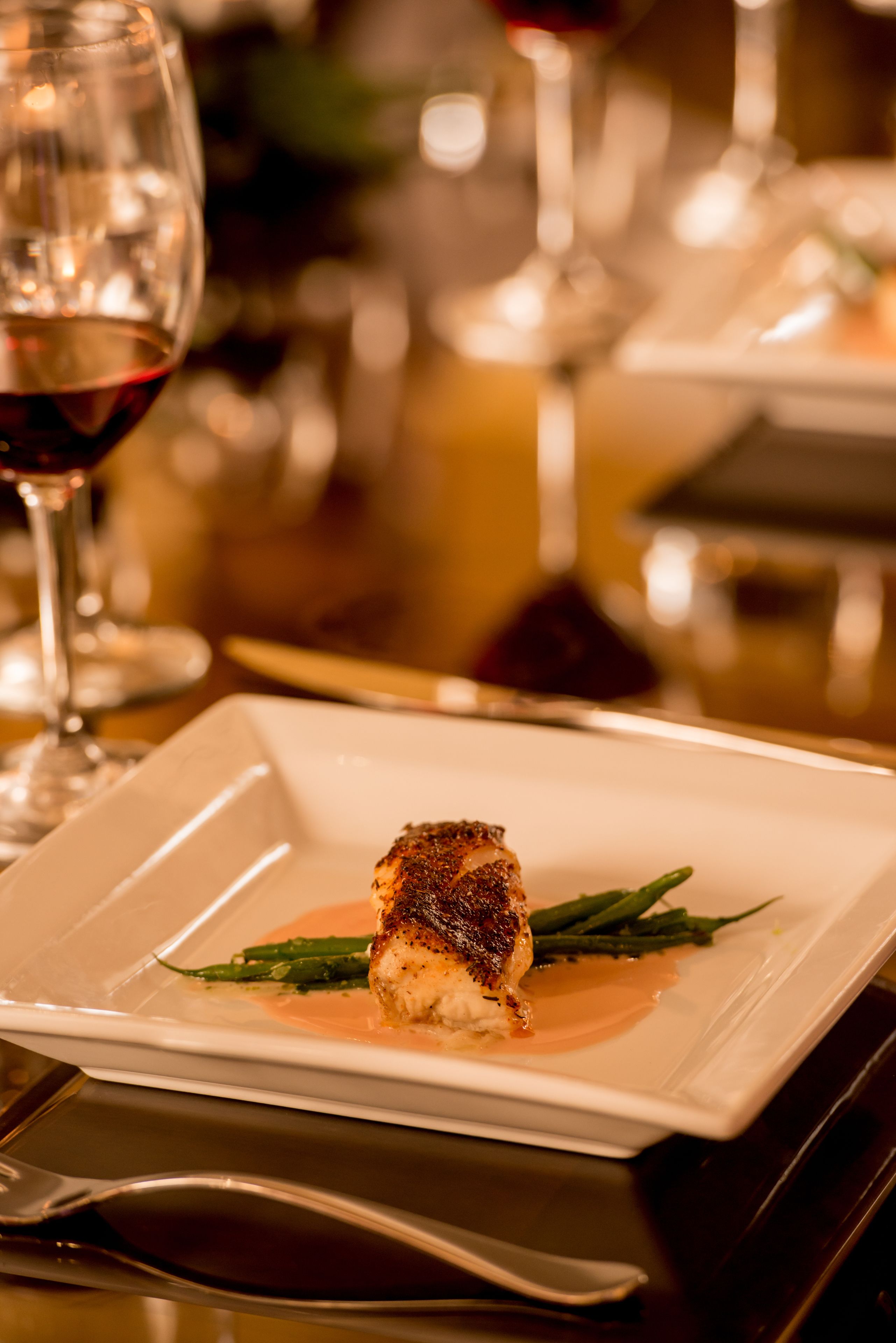 A square plate with a piece of grilled meat, green asparagus, and a sauce.