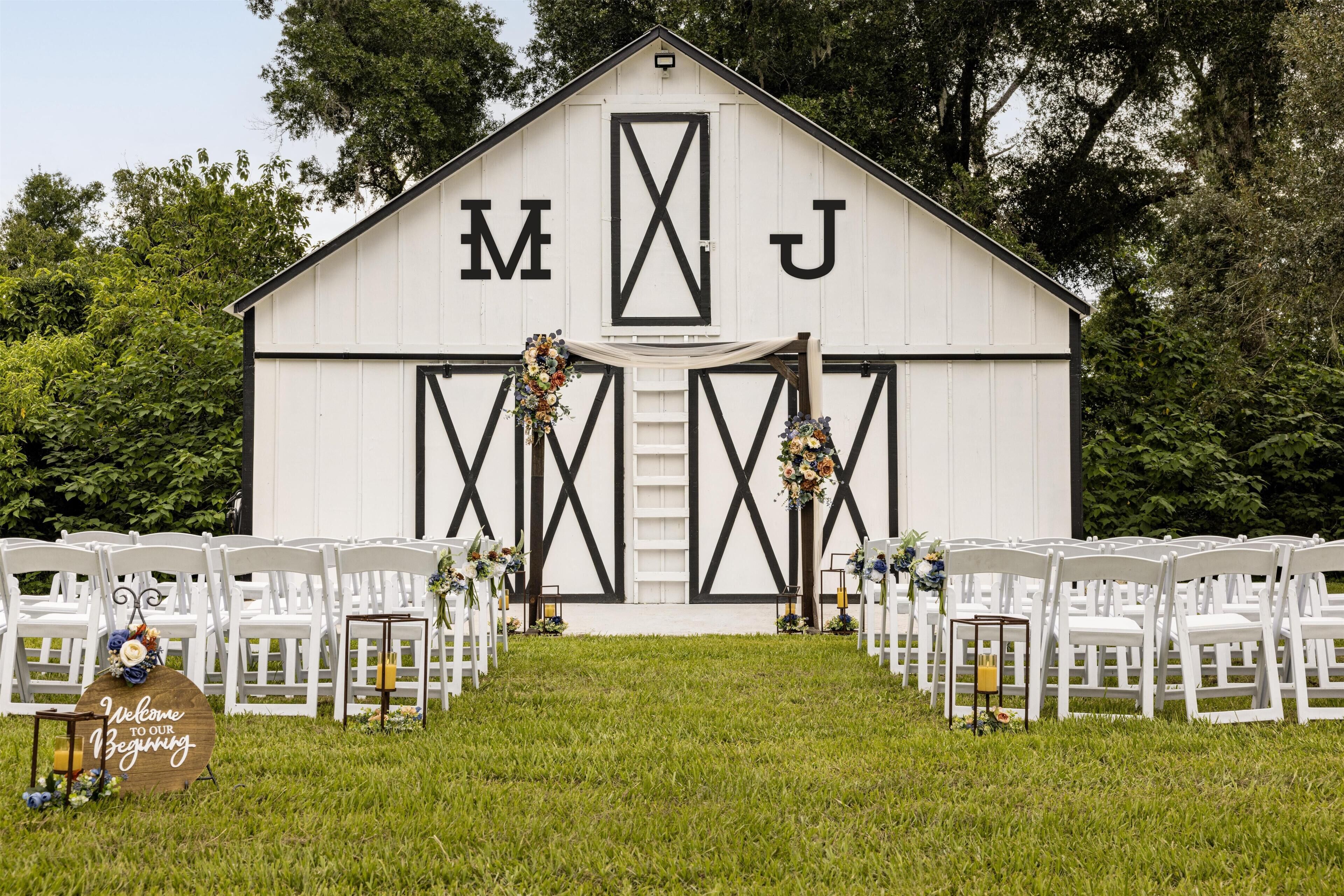 Un lieu de réception de style grange, avec une façade blanche et des éléments décoratifs noirs, où l’on peut voir les initiales « MJ » sur la devanture.