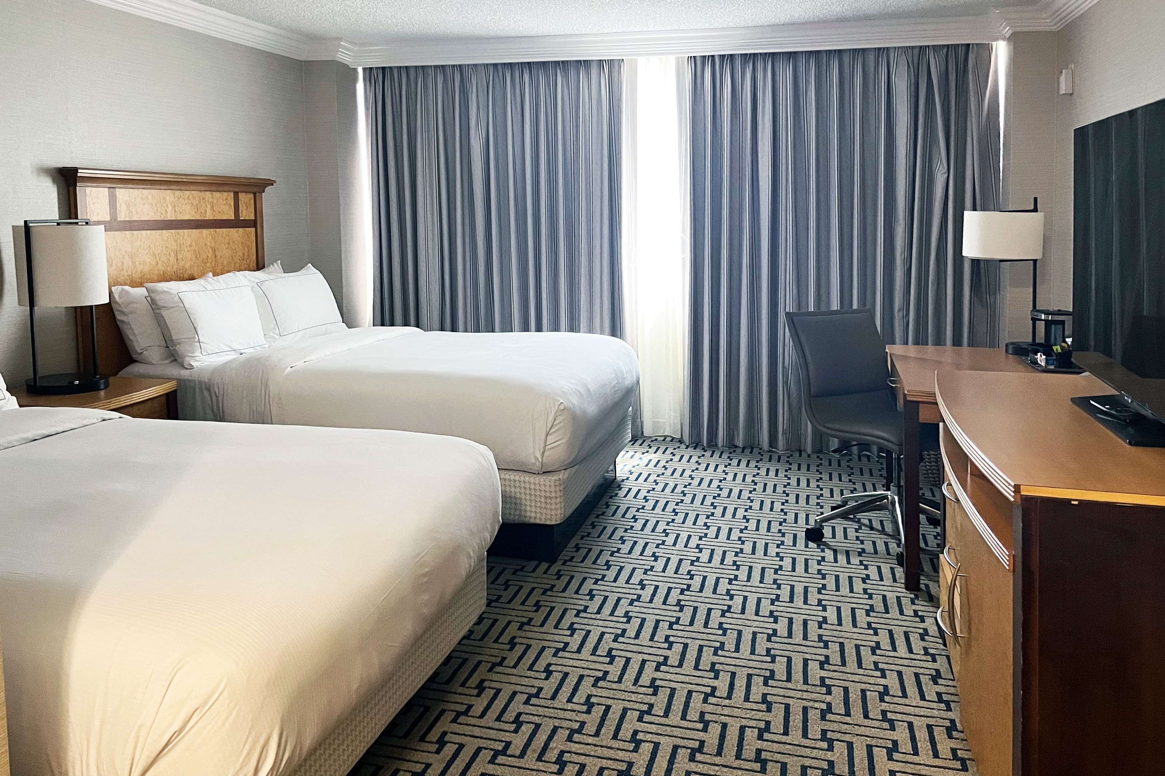 Habitación de hotel con dos camas, un escritorio, una silla, una lámpara y una alfombra estampada.