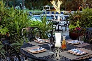 An outdoor dining area with round tables, chairs, and a pool in the background. - Hilton Ocala (Ocala)
