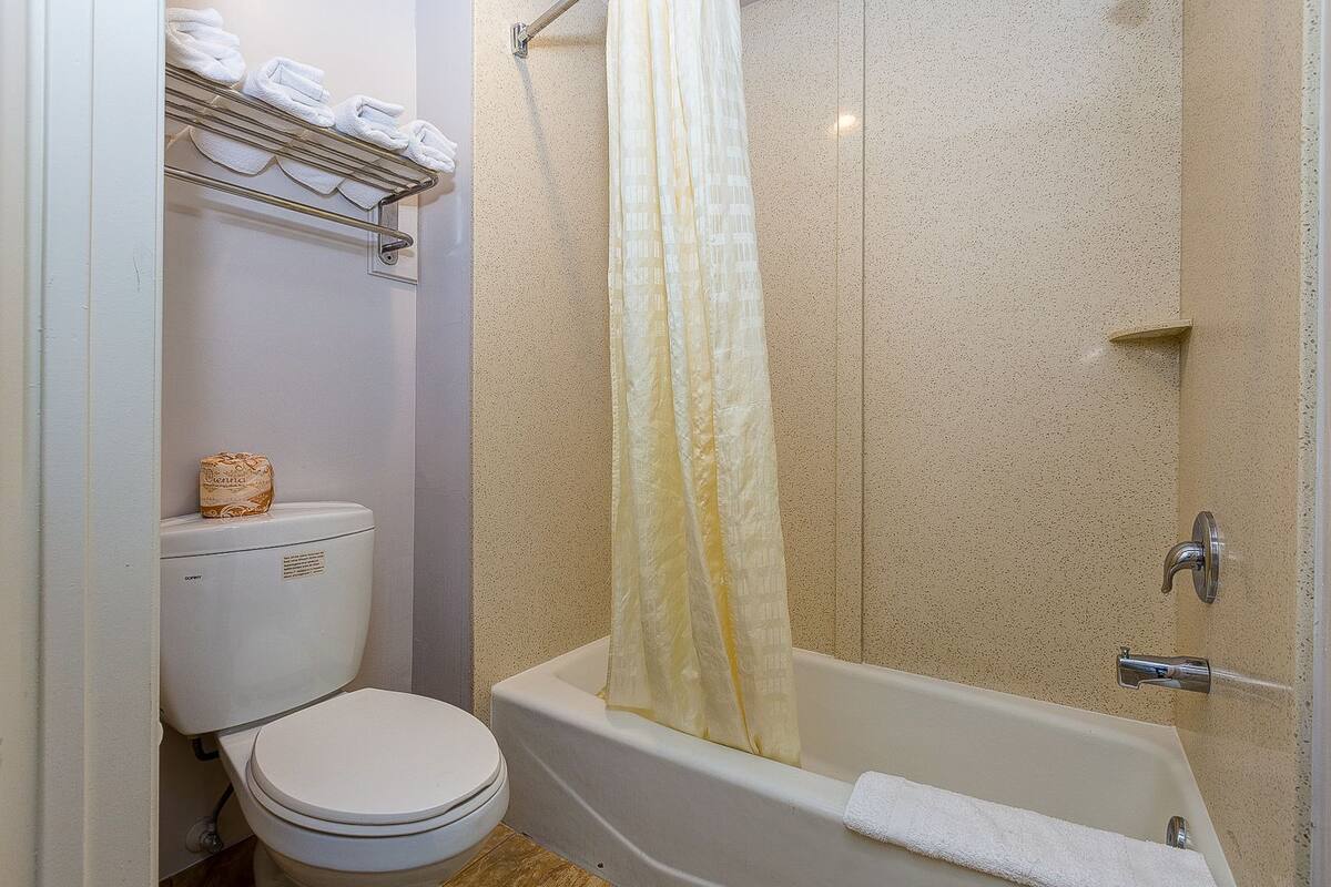 A bathroom with a toilet, a shower with a yellow curtain, and a shelf with folded towels.