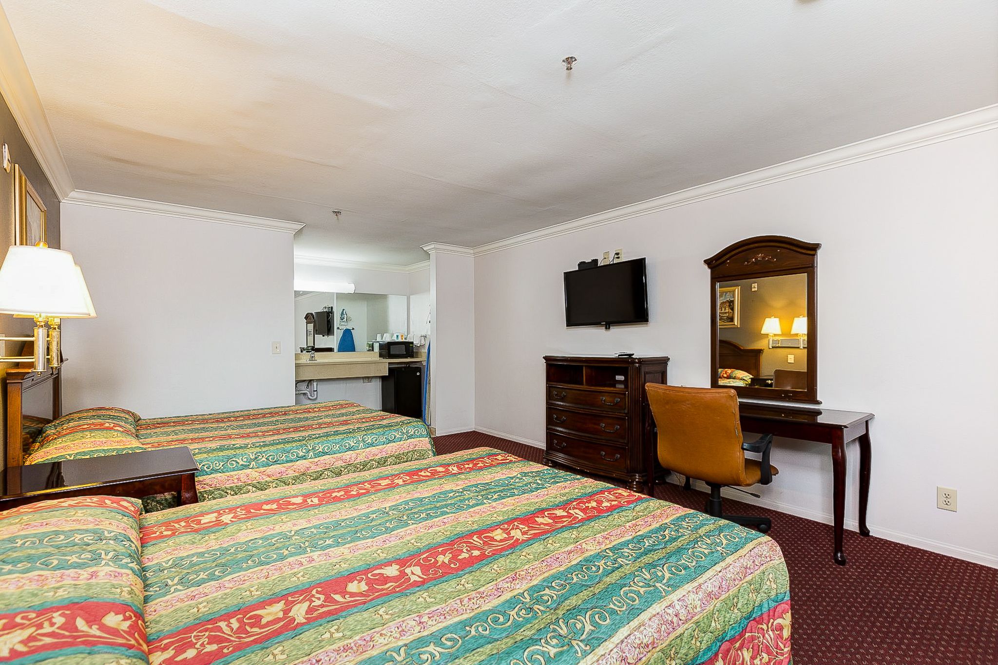 A hotel room with two beds, a desk, a chair, a television, and a mirror.