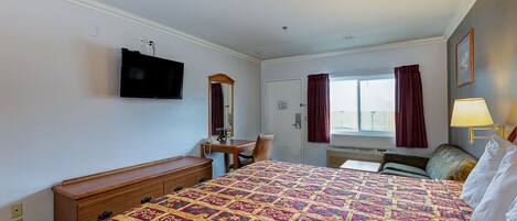 Una habitación de hotel con una cama grande, un escritorio, una silla, un televisor montado en la pared y una ventana con cortinas.