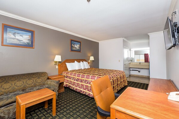 A hotel room with a bed, a sofa, a desk, and a chair. There are two lamps on either side of the bed.