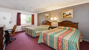 A hotel room with two beds, a desk, a chair, and a window with curtains. - Buena Vista Inn (Anaheim)