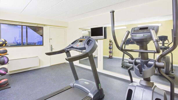 Ein Fitnessraum mit Laufbändern, Übungsbällen und einem Fernseher an der Wand.