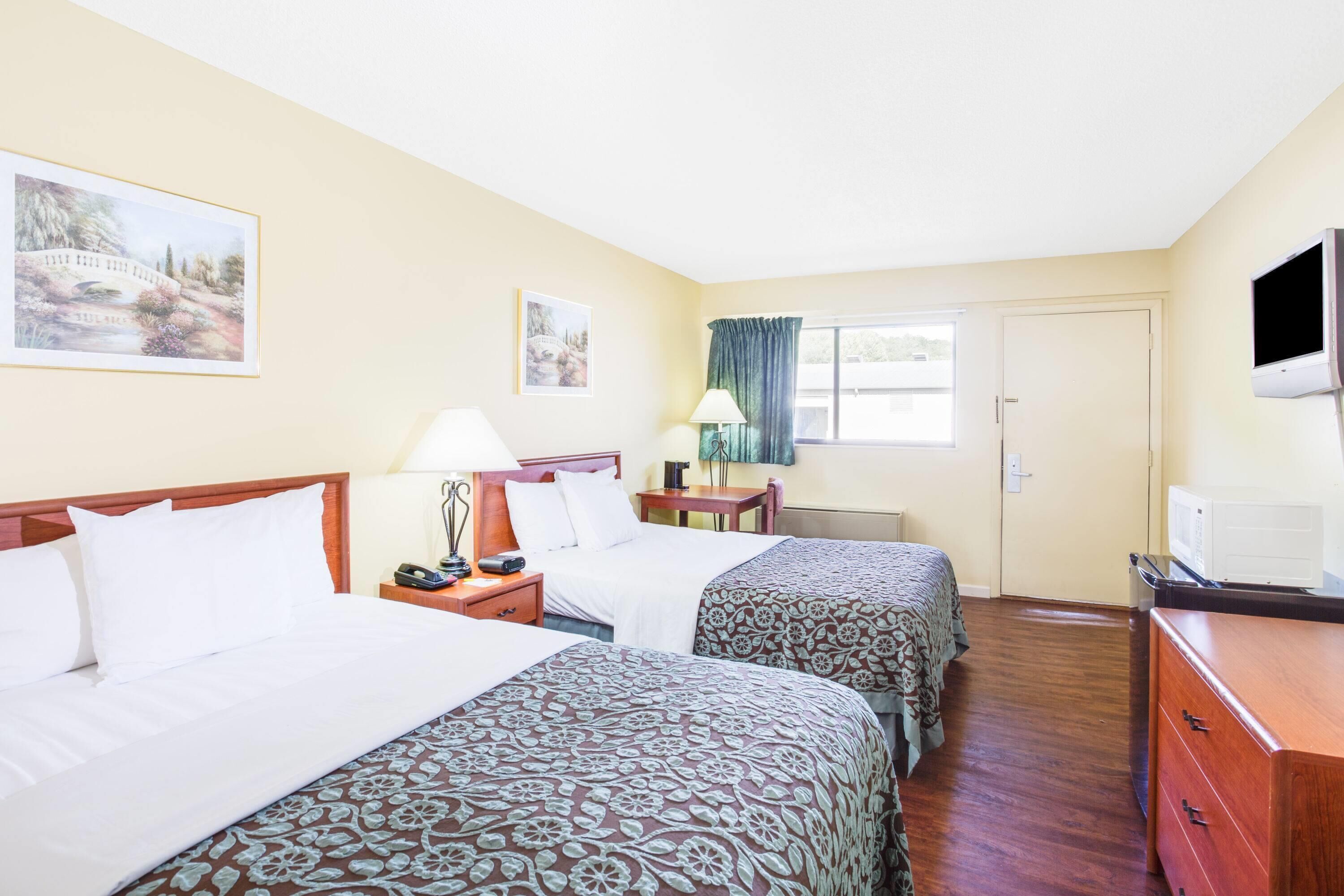 A hotel room with two beds, a desk, a television, and a window with curtains.