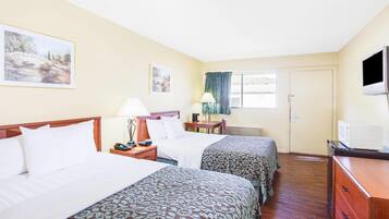 A hotel room with two beds, a desk, a television, and a window with curtains.