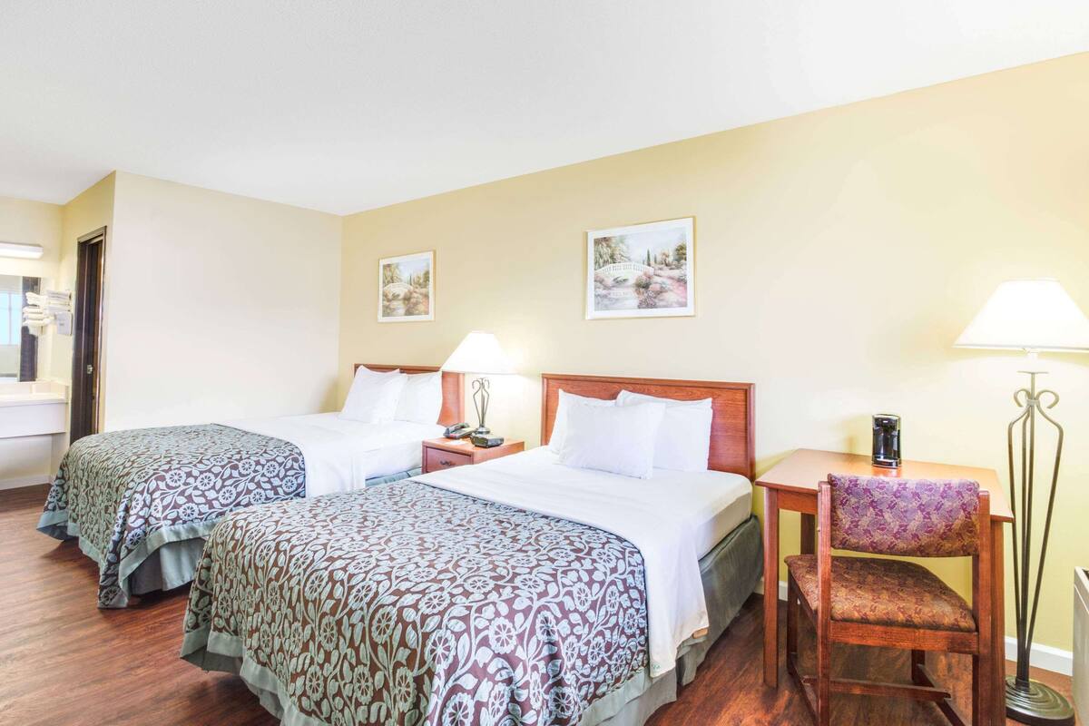 A hotel room with two beds, a small table, a chair, and a lamp.