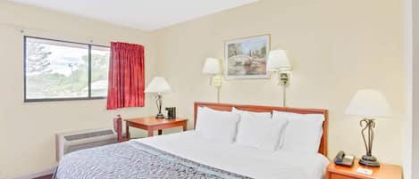 A hotel room with a large bed, two bedside tables, a window with a view, and a painting on the wall.