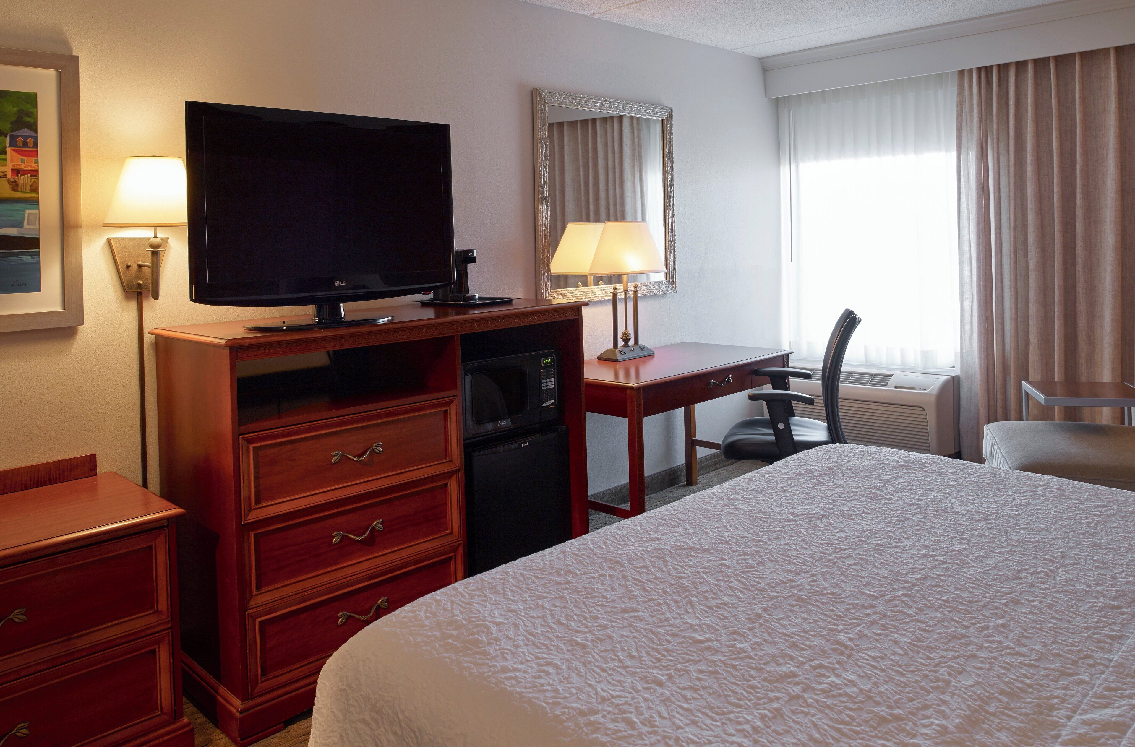 Una habitación de hotel con cama, televisión, escritorio con silla, microondas y lámpara.