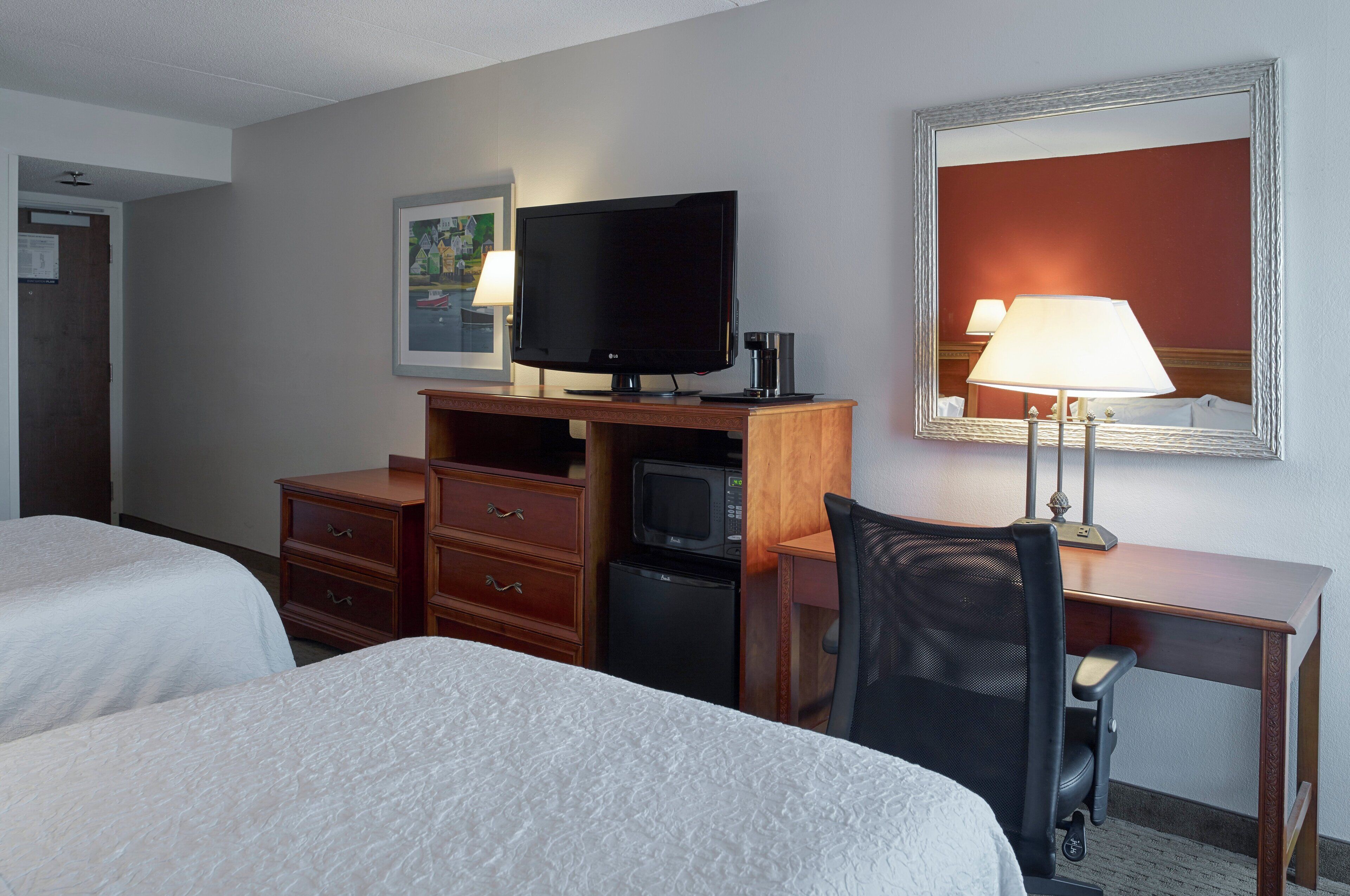 A hotel room with two beds, a desk with a computer, a television, a microwave, and a lamp.
