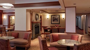 A hotel lobby with a fireplace, seating areas, and a hallway. - Long Creek Hotel by IHG (South Portland)