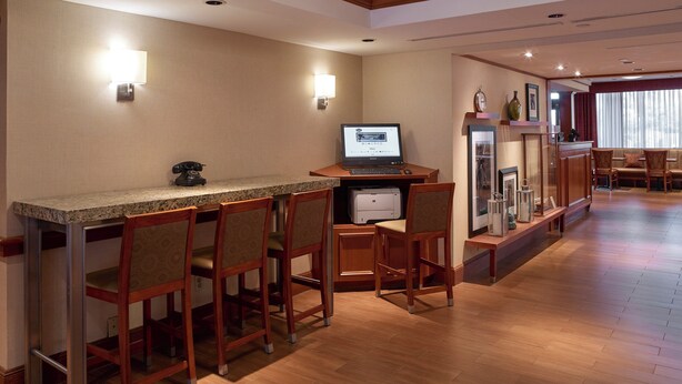 A hotel bar with a granite countertop, wooden chairs, a desktop computer, and a telephone. - Long Creek Hotel by IHG (South Portland)