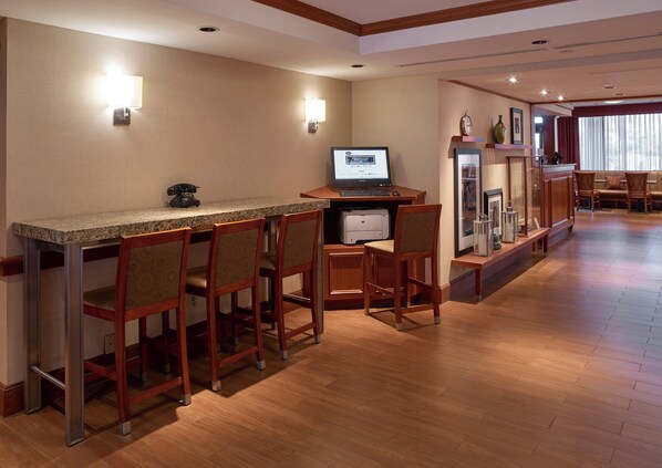 Un bar d’hôtel doté d’un comptoir en granit, de chaises en bois, d’un ordinateur de bureau et d’un téléphone.