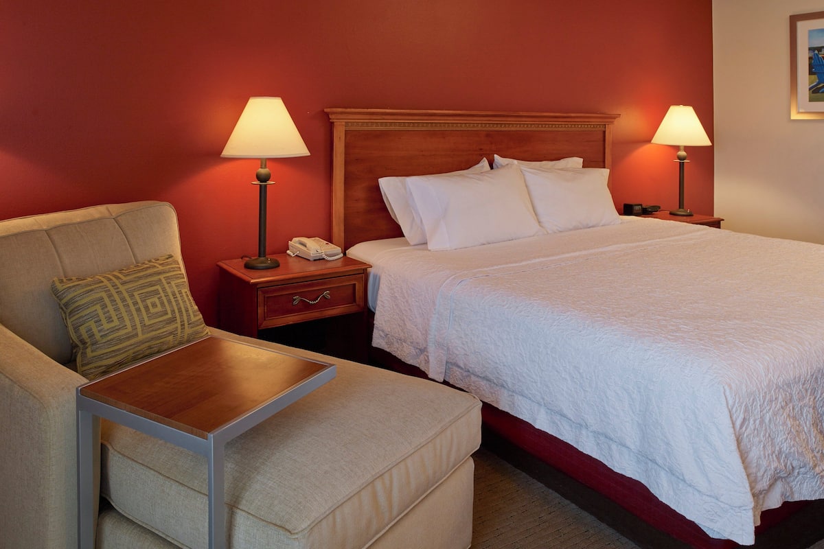 A hotel room with a bed, two bedside lamps, a telephone, a chair, and a small table.