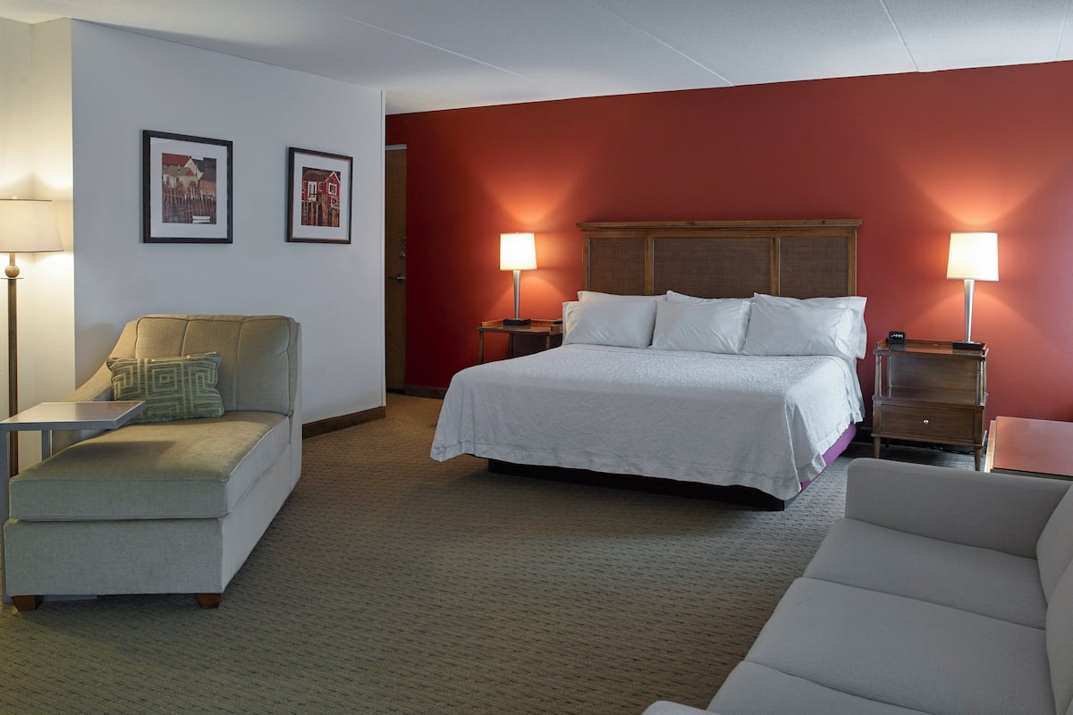 A hotel room with a bed, two bedside tables, a sofa, and two lamps.