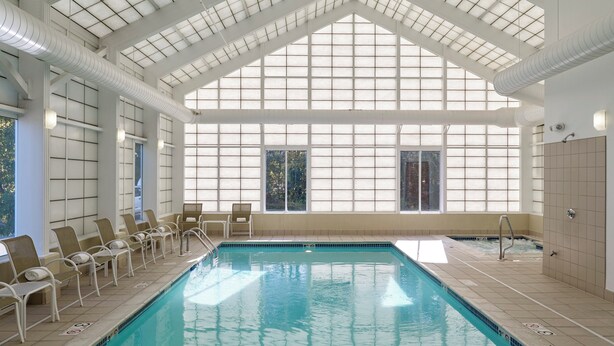 An indoor swimming pool with clear blue water, surrounded by lounge chairs and a high ceiling with skylights. - Long Creek Hotel by IHG (South Portland)