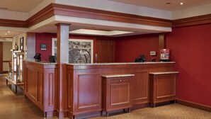 A reception area with a wooden reception desk, a framed picture on the wall, and a red carpeted floor. - Long Creek Hotel by IHG (South Portland)