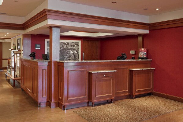 A reception area with a wooden reception desk, a framed picture on the wall, and a red carpeted floor.