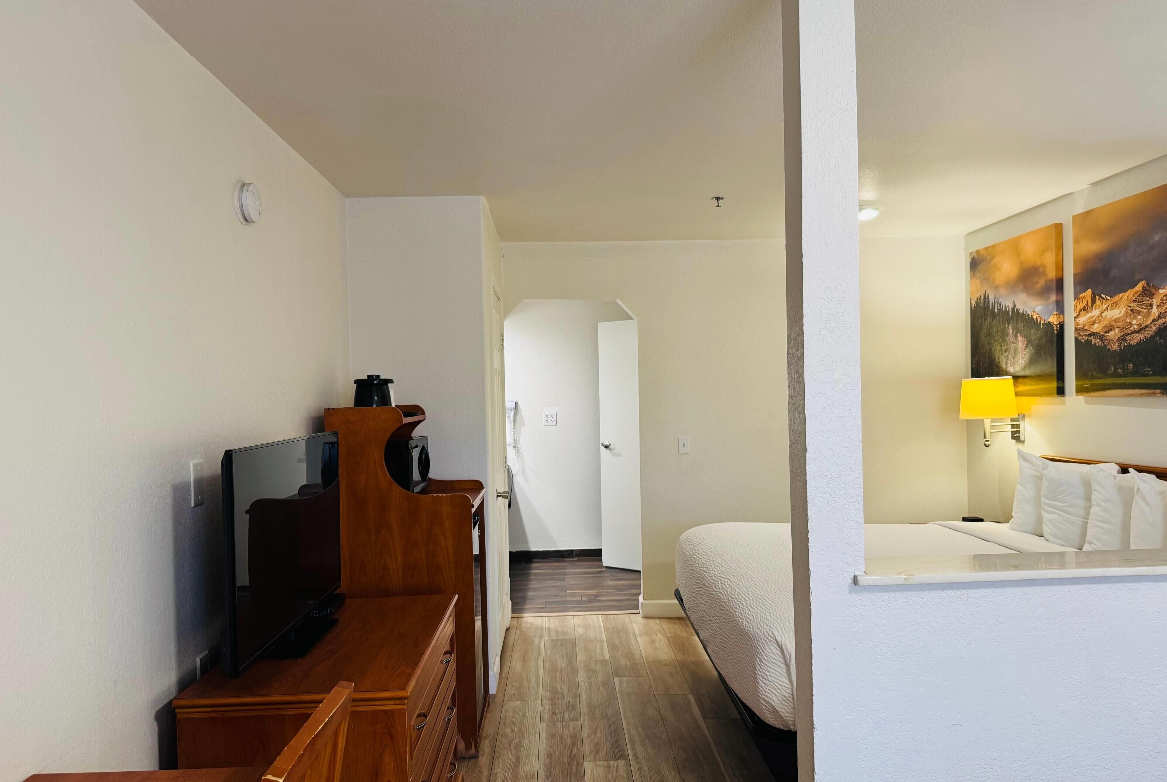 A hotel room with a TV, wooden furniture, a bed, a painting, and a lamp.