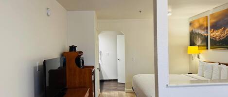 A hotel room with a TV, wooden furniture, a bed, a painting, and a lamp.