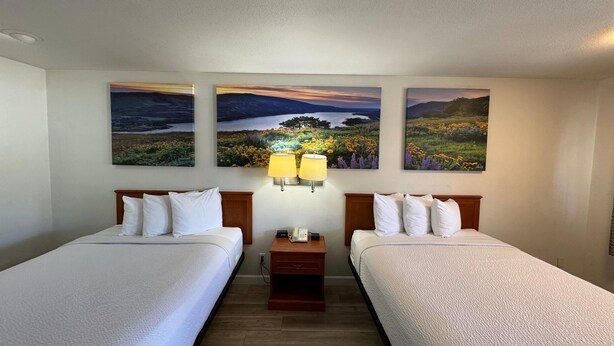 A hotel room with two beds, a nightstand with a lamp, and three landscape paintings on the wall. - Days Inn by Wyndham Bishop (Bishop)