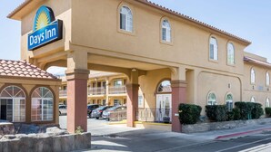 A Days Inn with a beige facade, arched windows, and a parking lot with several cars. - Days Inn by Wyndham Bishop (Bishop)