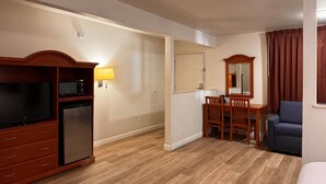 A hotel room with a wooden cabinet, a television, a small refrigerator, a desk with a chair, a mirror, and a sofa. - Days Inn by Wyndham Bishop (Bishop)