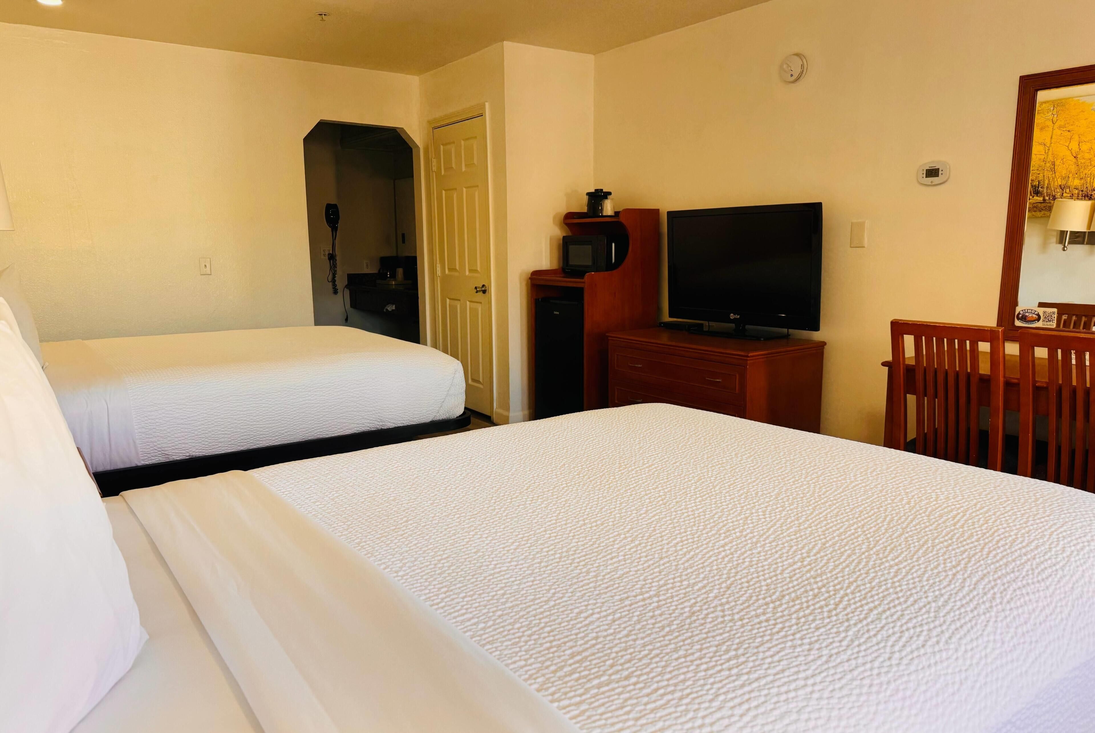 A hotel room with two beds, a television, a microwave, and a desk.