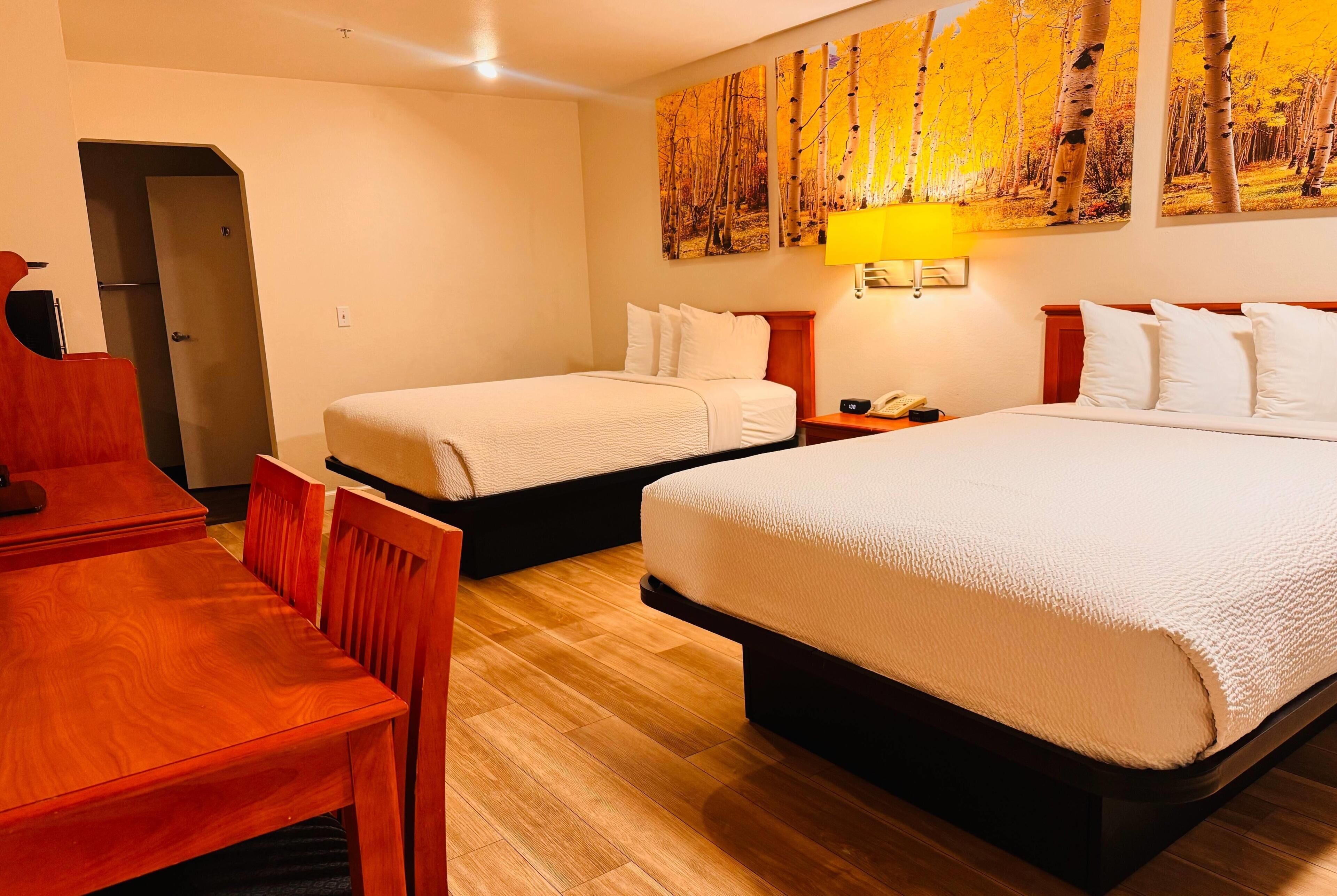 A hotel room with two beds, a wooden desk, and a chair.