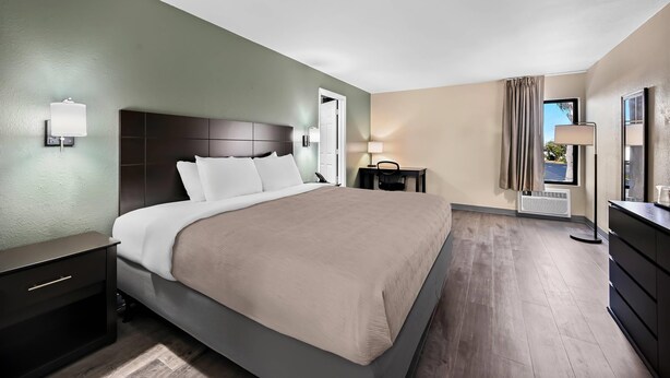 A hotel room with a large bed, bedside tables, a desk, and a window with curtains.