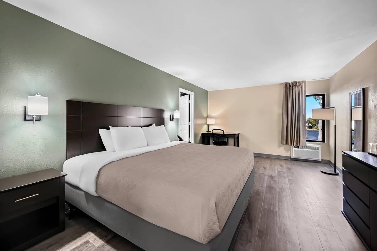 Una habitación de hotel con una cama grande, mesitas de noche, un escritorio y una ventana con cortinas.