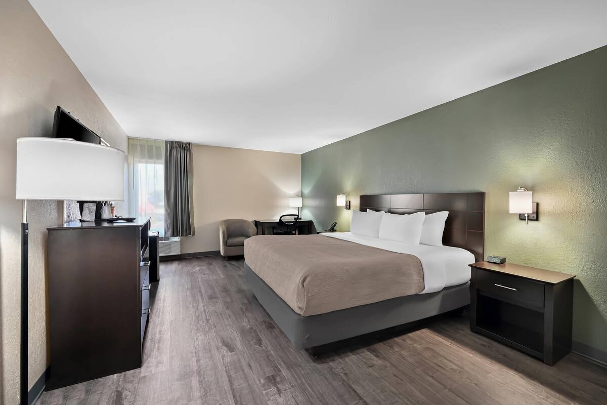 Una habitación de hotel con cama, mesitas de noche, escritorio, silla y lámpara.