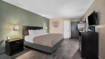 Habitación de hotel con cama, mesita de noche, lámpara, una obra de arte y televisor sobre un soporte.