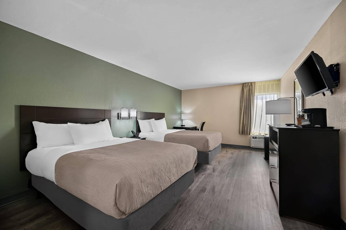 Habitación de hotel con dos camas, un escritorio, una silla, un televisor y una ventana con cortinas.
