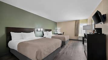 Habitación de hotel con dos camas, un escritorio, una silla, un televisor y una ventana con cortinas.