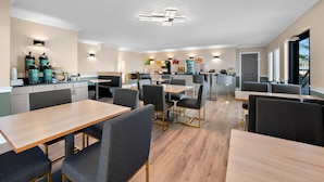 Een moderne hotelkeuken met een centraal eiland, een bar met zitplaatsen en een eethoek met tafels en stoelen.