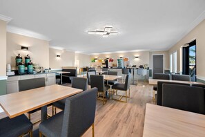 A modern hotel kitchen with a central island, bar seating, and a dining area with tables and chairs. - Quality Inn Fort Myers Cape Coral (Fort Myers)