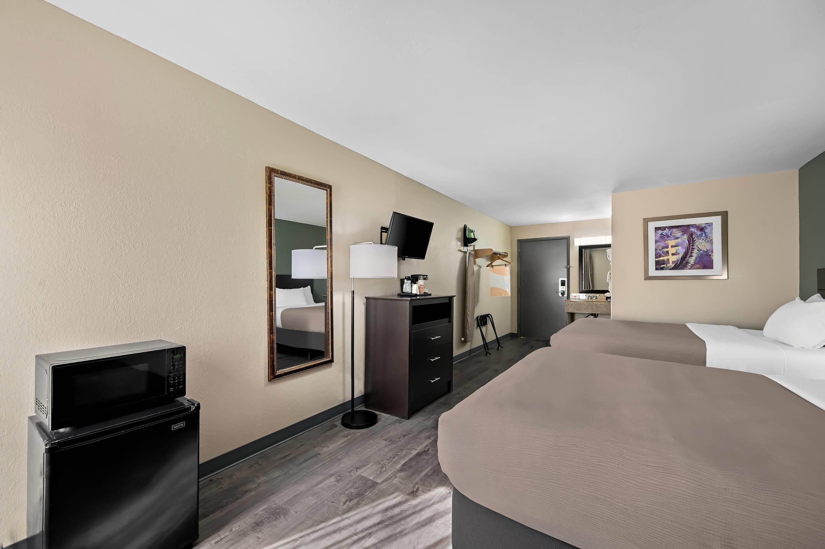 Habitación de hotel con cama, escritorio con computadora, microondas, televisión y espejo.