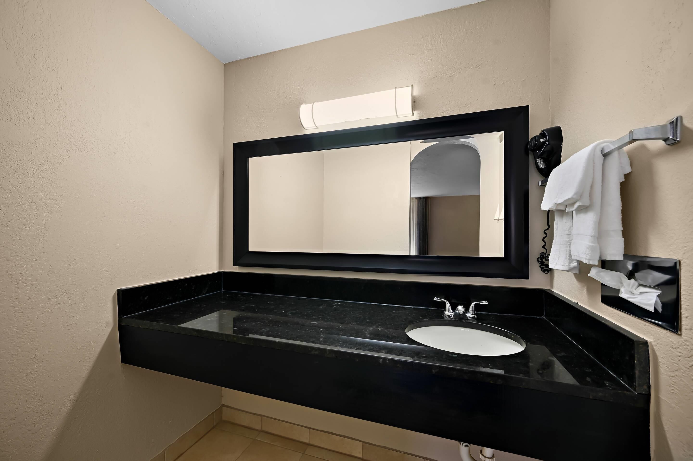 A modern bathroom with a black sink, a large mirror, and a towel rack.