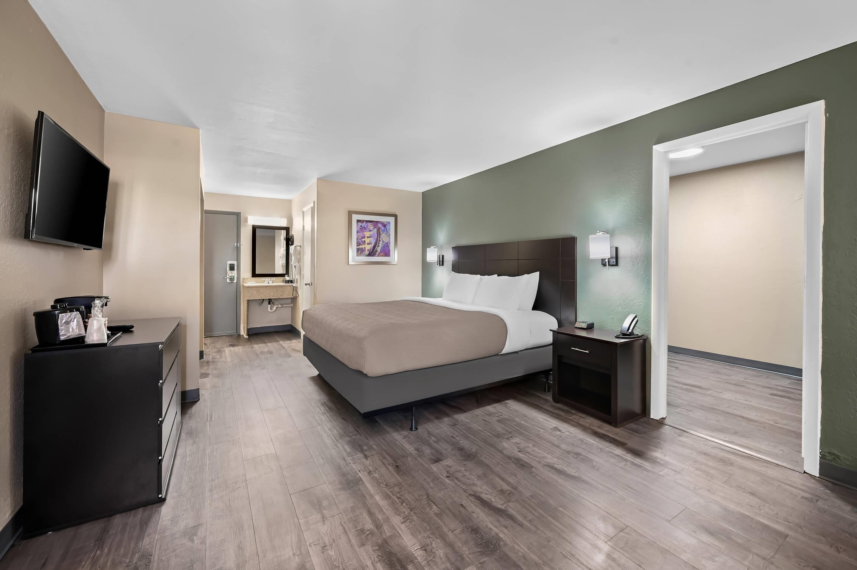 Una habitación de hotel moderna con una cama grande, un televisor de pantalla plana, un aparador y una puerta que da a otra habitación.