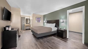 Una habitación de hotel moderna con una cama grande, un televisor de pantalla plana, un aparador y una puerta que da a otra habitación.