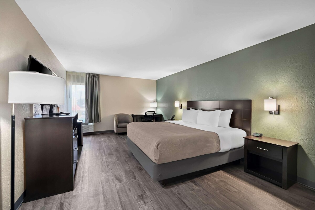 A hotel room with a bed, bedside tables, a desk, a chair, and a lamp.