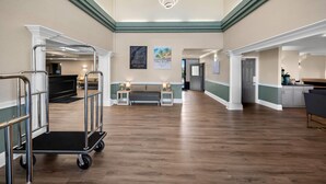 A spacious hotel lobby with a wooden floor, a reception desk, a sofa, and a cart.