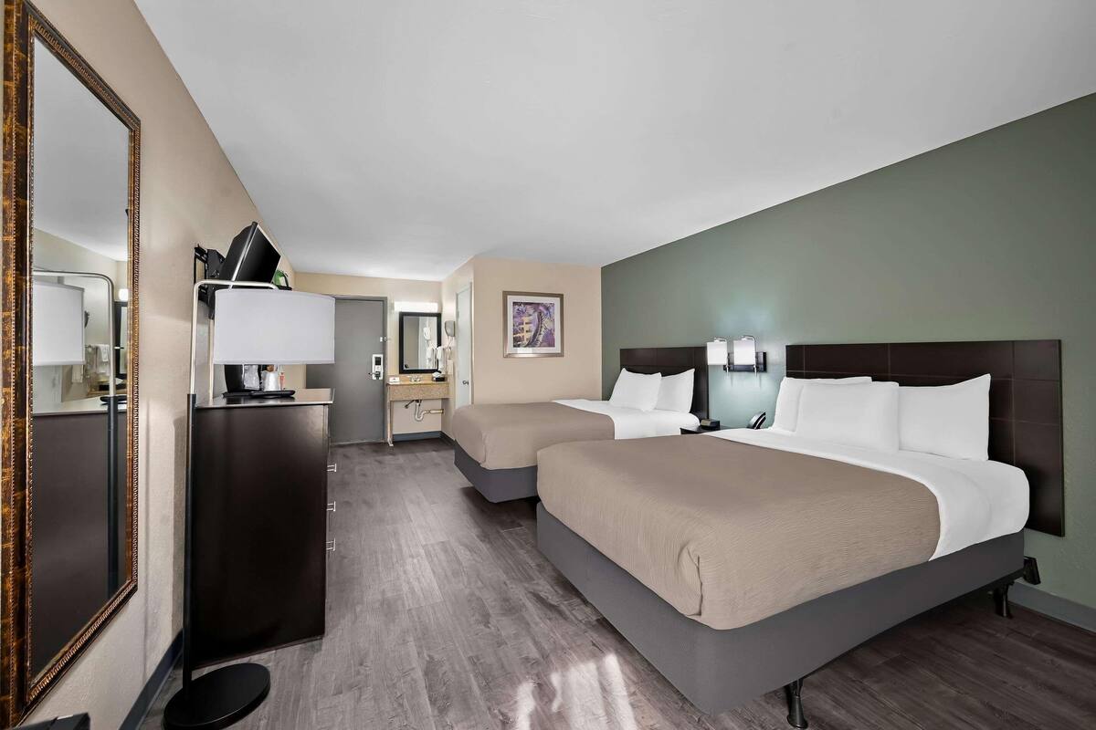 A hotel room with two beds, a dresser, a mirror, a desk with a lamp, and a framed picture on the wall.