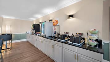 A kitchen with a long counter, a refrigerator, a coffee machine, and a microwave.