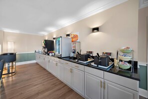 A kitchen with a long counter, a refrigerator, a coffee machine, and a microwave.