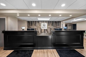 A hotel reception area with two reception desks, a sign reading 'Quality by Choice Hotels', and a 'WELCOME!' sign on the wall.